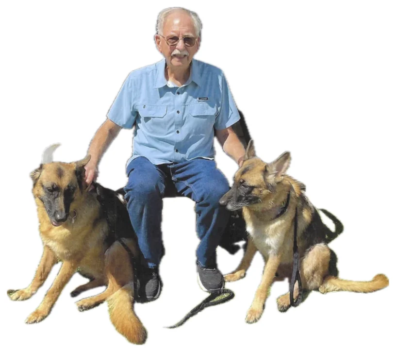 Ron Cable, smiling in a blue shirt, sitting between his two German Shepherds